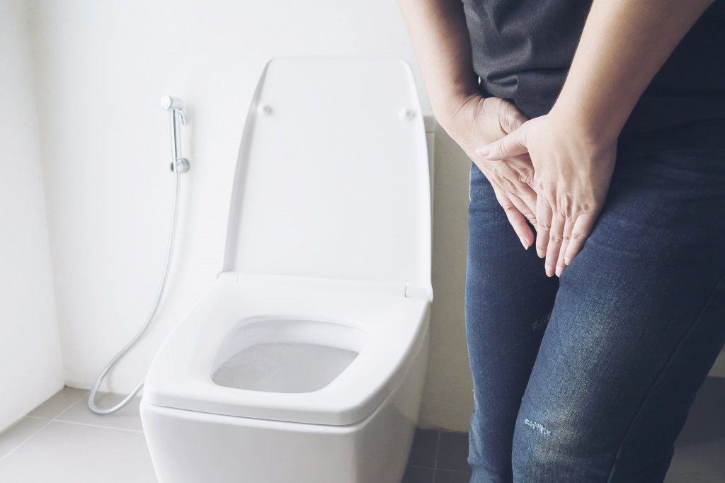 Женщина находится в туалетной комнате и держится за промежность руками из-за болей и резей в области мочевого пузыря